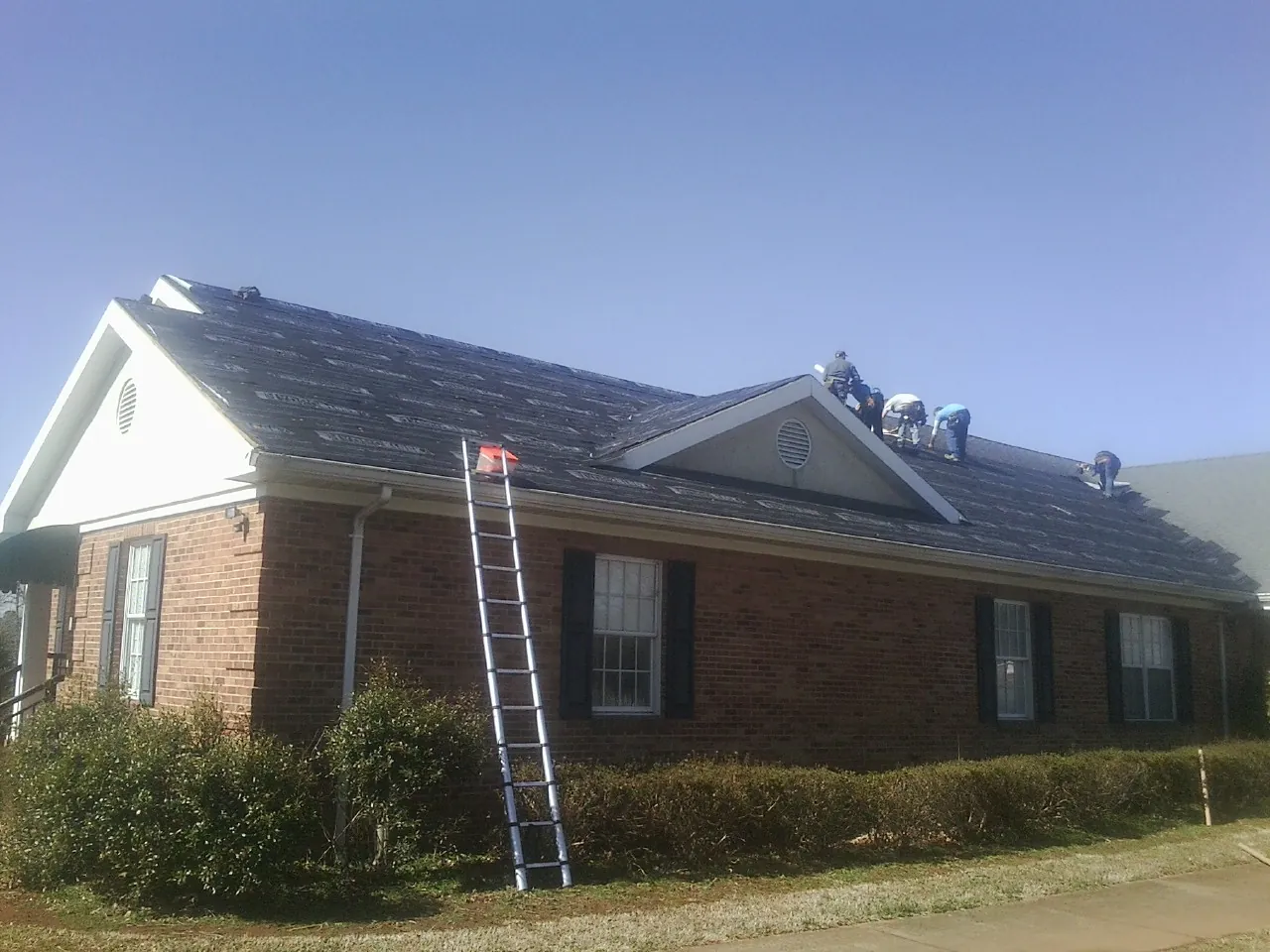 Crew tearing shingles off a brick ranch roof with a ladder set — Metal Roof Repair work by our crew in Sturbridge