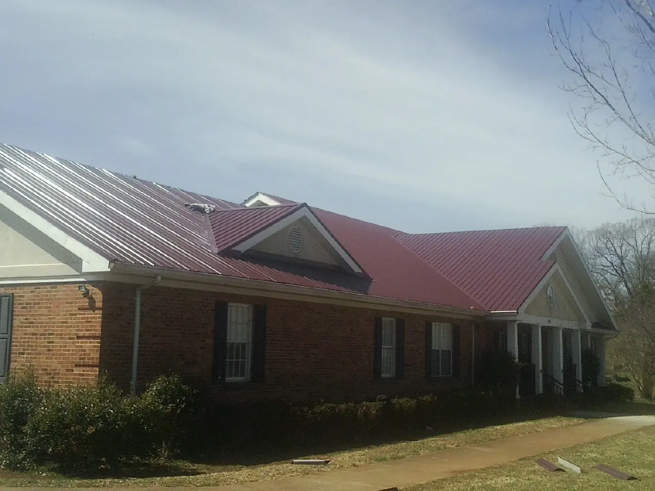Red metal roof with gabled entries on a long brick building, from a Hail Damage Roof Repair job in Sturbridge