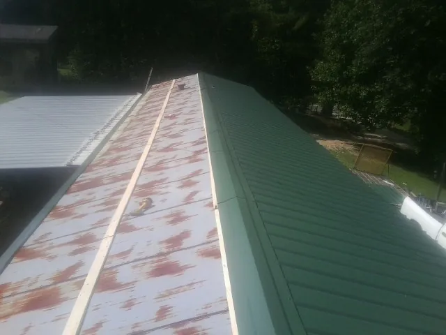 Old rusted panels beside newly installed green metal roofing — Wind Damage Roof Repair by Roofing Brothers in Sturbridge