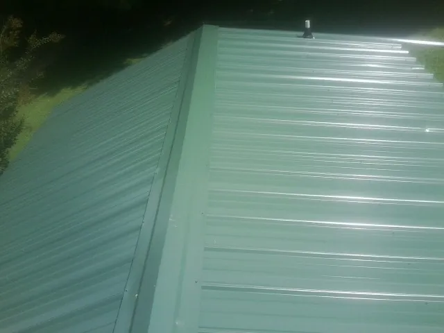New green metal panels meeting at the ridge of a roof — Flat Roof Repair work by our crew in Sturbridge
