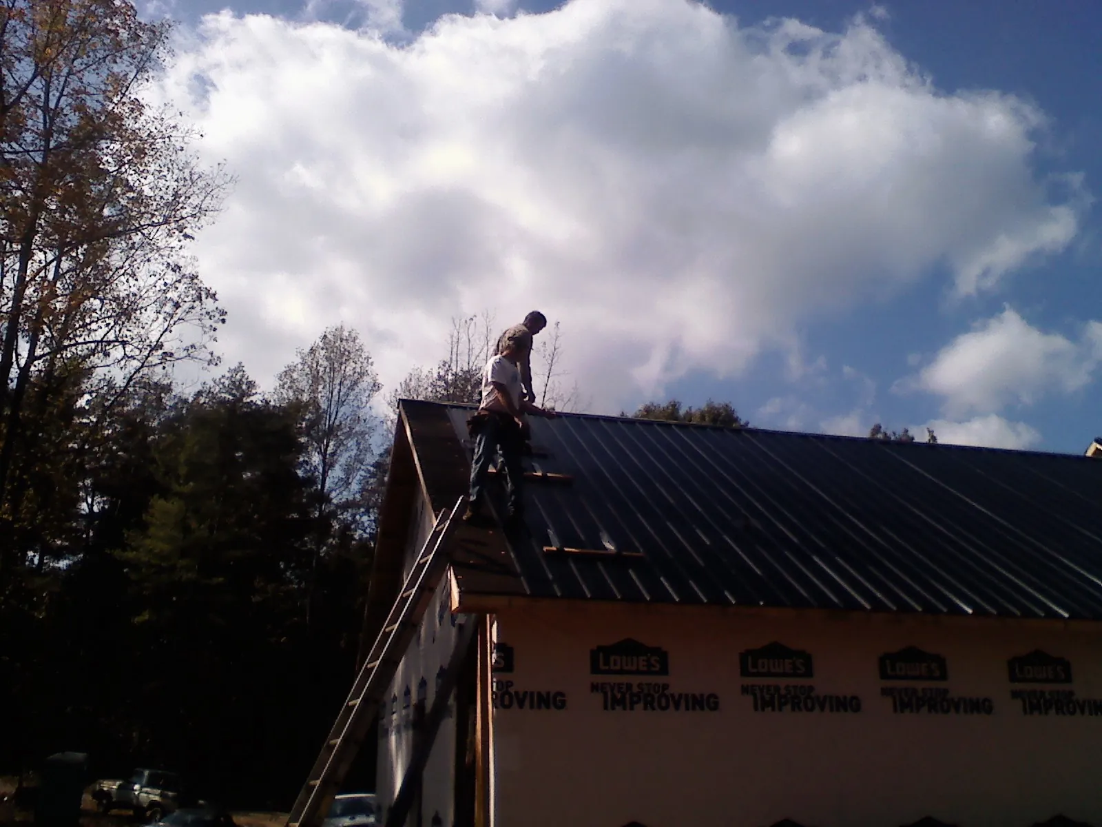 Roofer fastening dark metal panels high against a cloudy sky, from a Roof Inspection job in Sturbridge