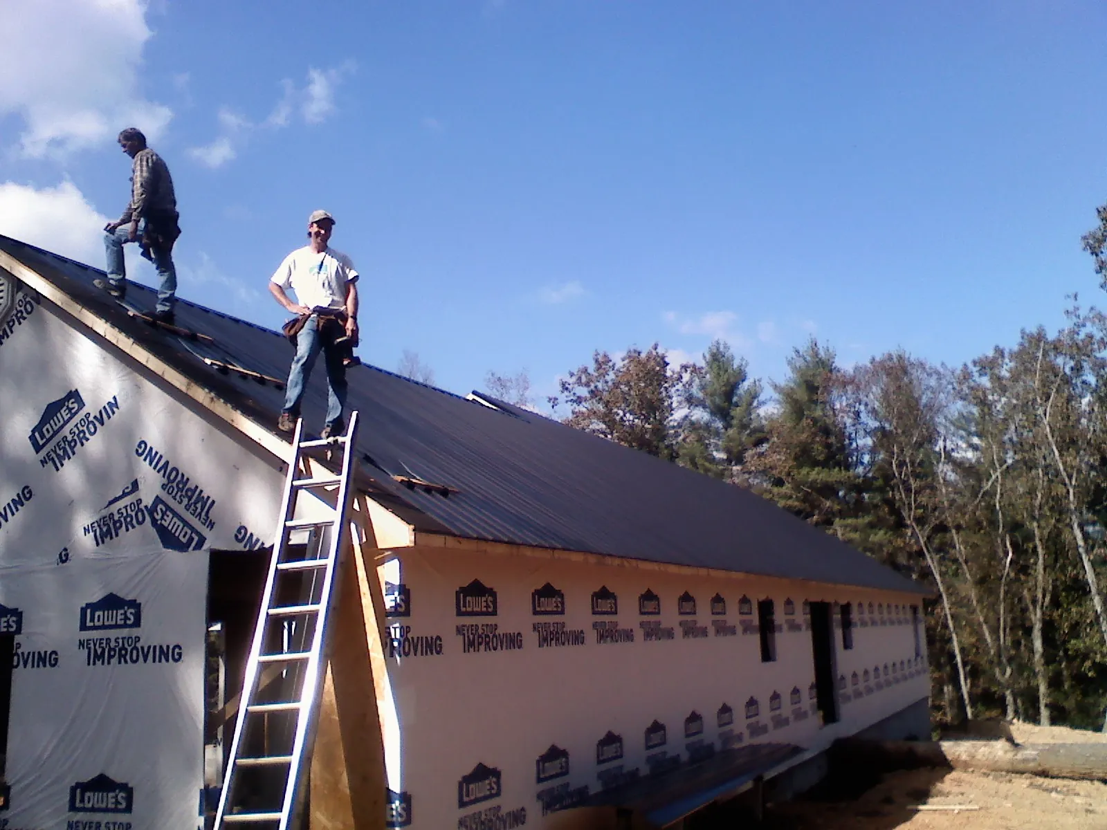 Two roofers standing on a long dark metal roof over a wrapped building in Sturbridge