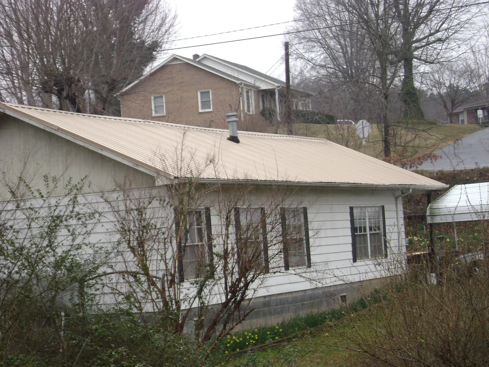 Tan metal roof on a white sided house set into a hillside — Commercial Roofing by Roofing Brothers in Sturbridge
