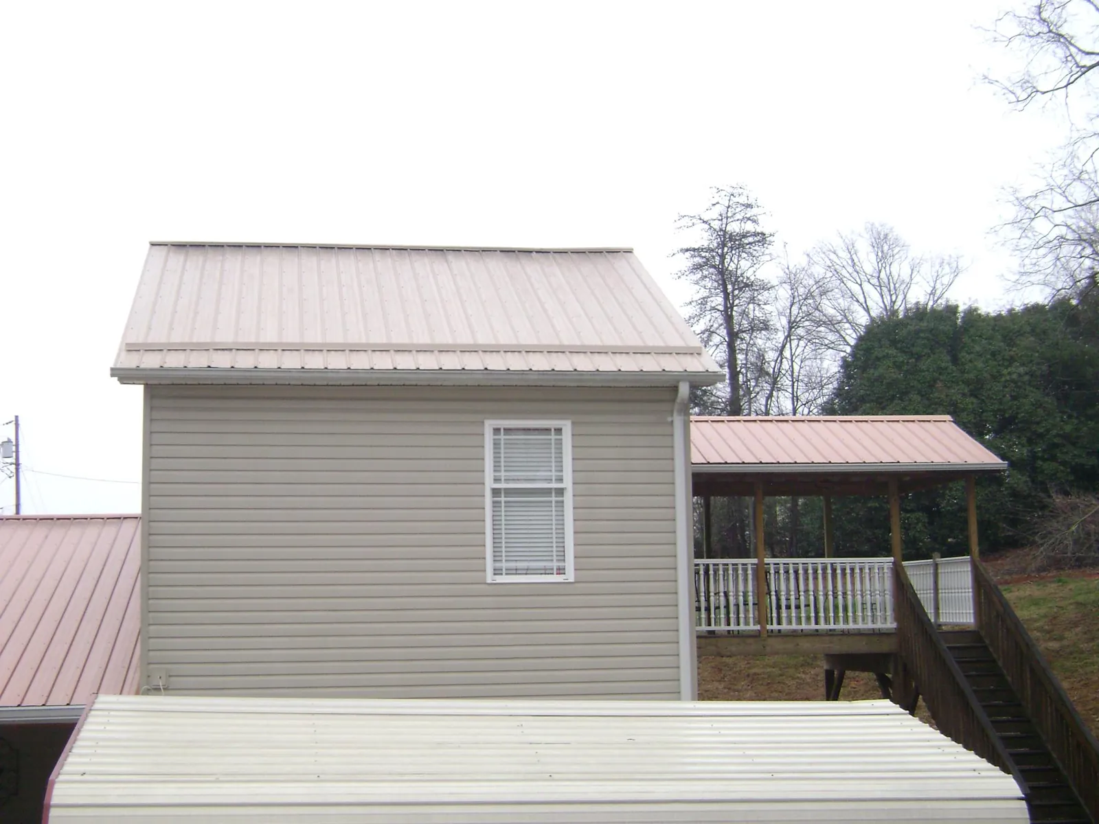 Tan metal roofs on a two story addition and attached porch, from a Roof Replacement job in Sturbridge