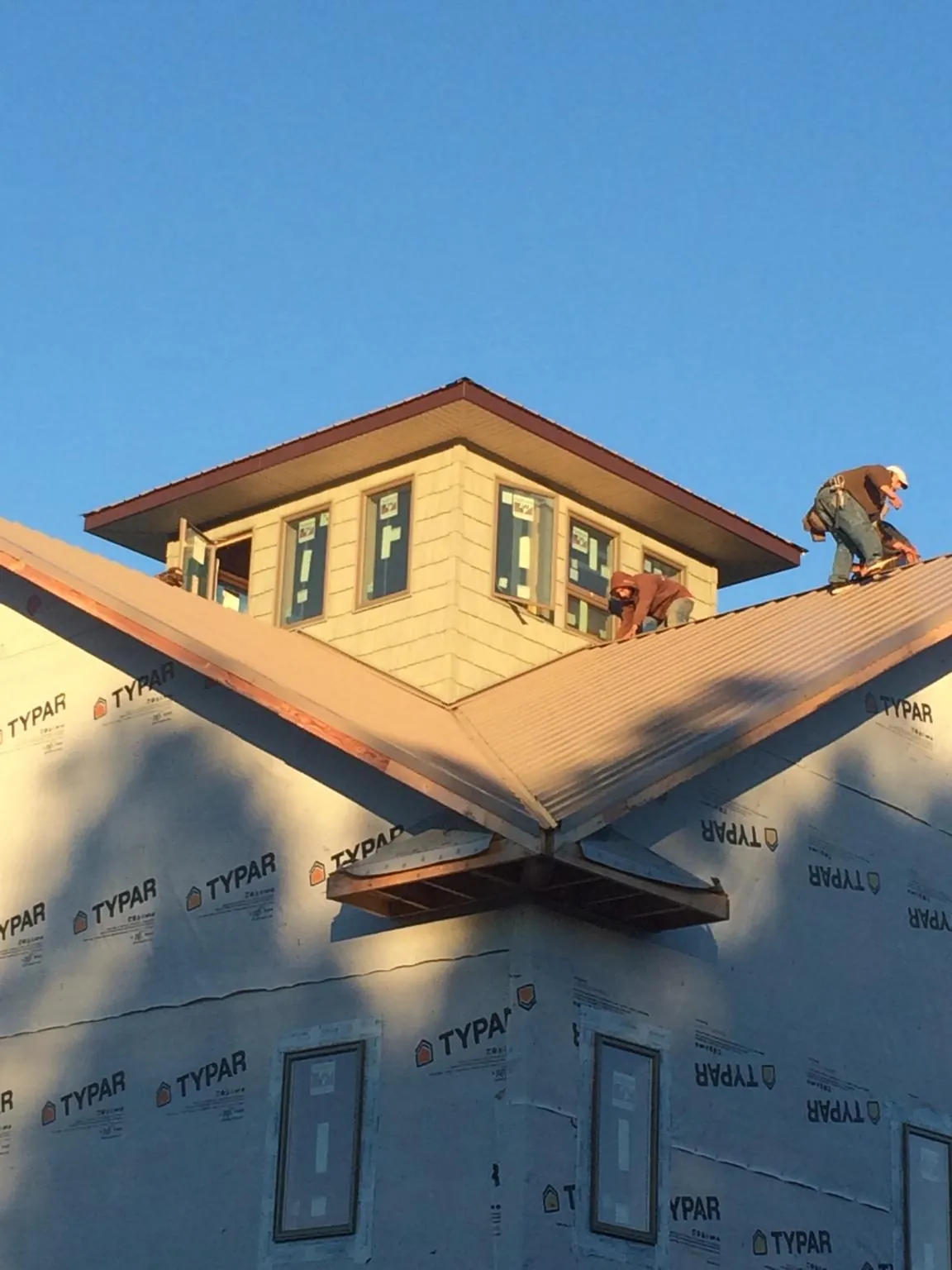 Roofers working around a rooftop cupola on a new metal roof at sunset — Roof Waterproofing in Sturbridge by Roofing Brothers